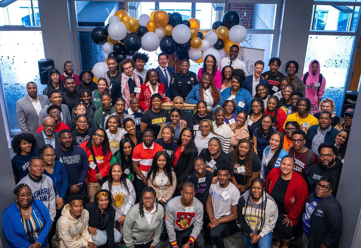 A large, diverse group of people posing together in a room decorated with black, white, and gold balloons.