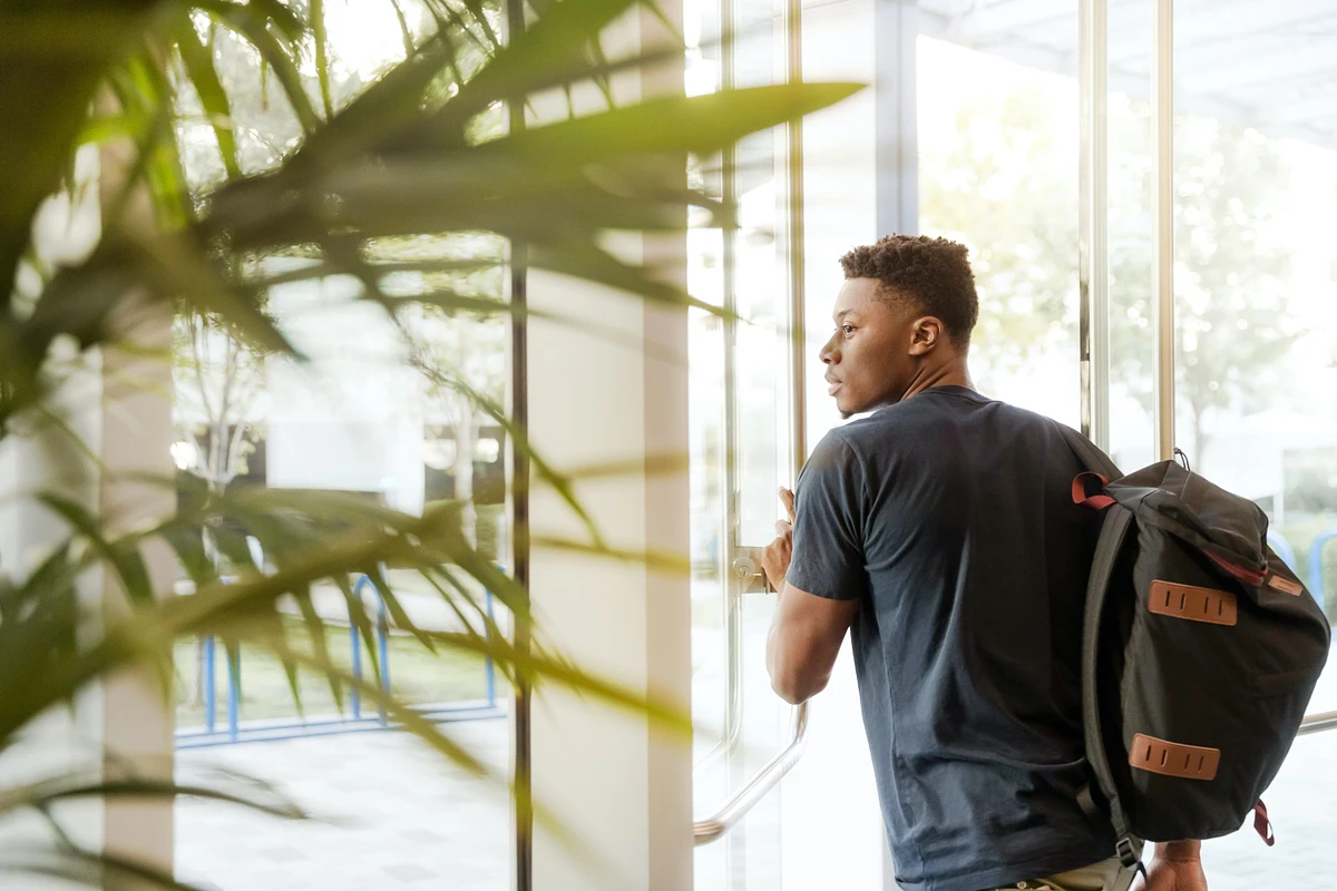 Young man approaching door to leave a building, green plant to the left