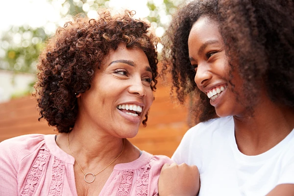 Two people are smiling at each other outdoors, sharing a joyful moment.